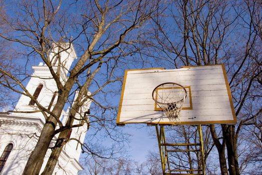 Old basketball board with an old tattered basketball net on the hoop near church.