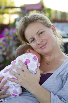 Tired mom holding her baby and relaxing outside after her baby turns week old.