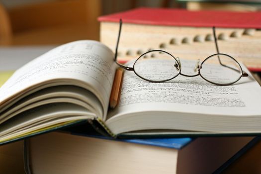 Text books on table with glasses and pencil
