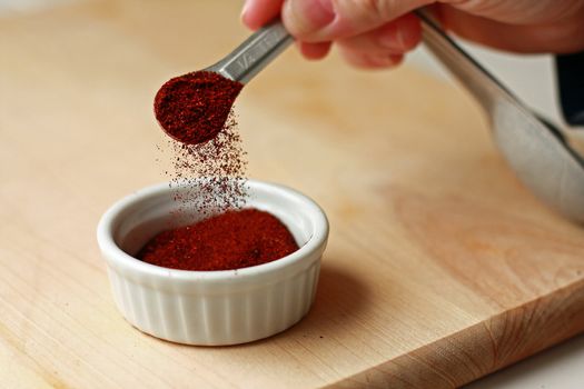 Spice measured with measuring spoon into ramekin on cutting board