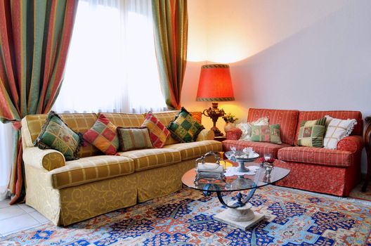 Elegant living room with classic looking sofa, colorful curtains, lamp and glass table