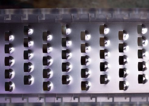 Close up of the slots in a stainless steel cheese grater lit from the side with color lights