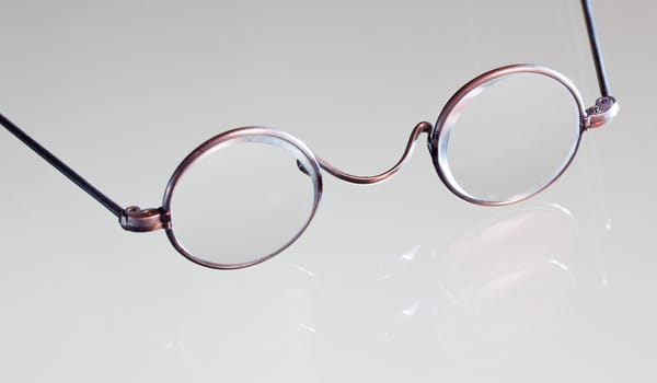 Old fashioned round reading glasses laying on a glass table and reflecting in the surface