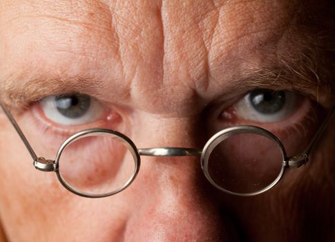 Portrait of a senior male with the focus on magnifying glasses and the eyes are blurred to suggest poor vision