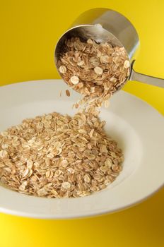 Measuring cup pouring organic cereal on white plate over colorful yellow background