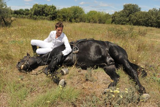 young man and his black stallion in  a field