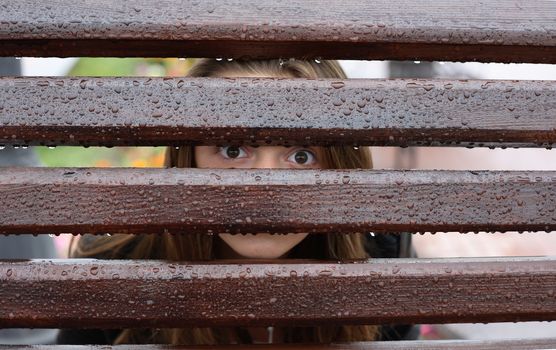 Teen girl looking through wet fence with water drops