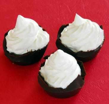 three chocolate treats with whipped cream over red background