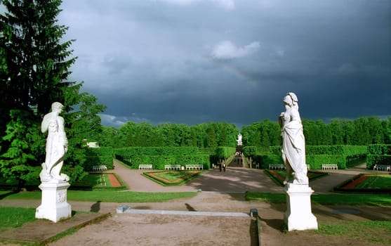 Classical statues in park and rainbow on dark sky