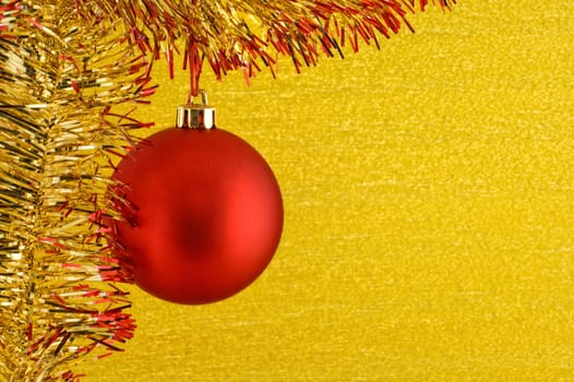 Red Christmas bauble hanging from glittering tinsel on golden background. Copy space for text.