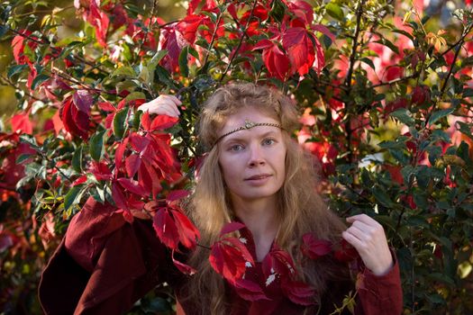 The blonde girle in medieval red dress in the autumn forest
