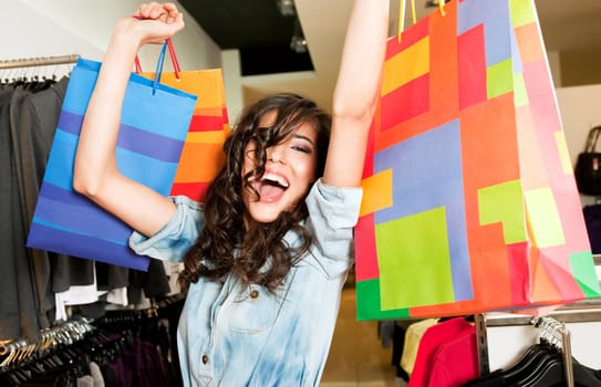 Beautiful happy female in store raising colourful shopping bags with excitement