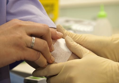 Close-up of nurse hands with gloves putting bandage plaster on patient vein
