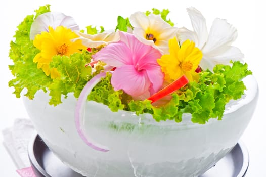 Green salad with tomatoes and various edible flowers in a bowl of ice on a white background