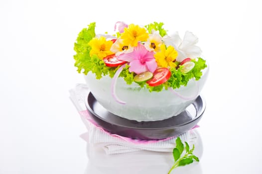 Green salad with tomatoes and various edible flowers in a bowl of ice on a white background