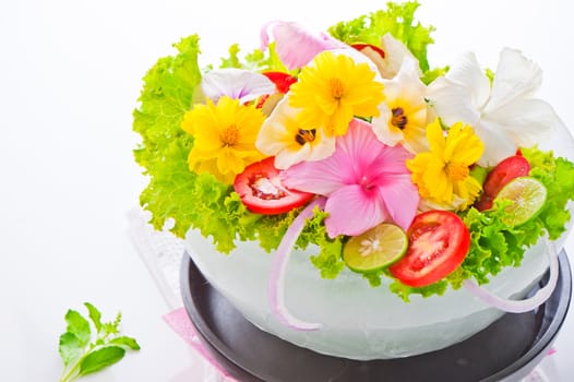 Green salad with tomatoes and various edible flowers in a bowl of ice on a white background