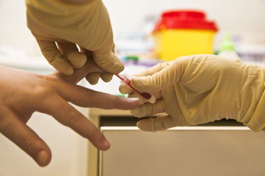 Close-up of hands with gloves taking blood sample from finger
