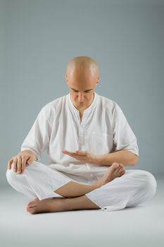 Male dressed in white sitting in meditation position, looking down