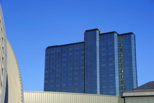 A glass-fronted building towering above lower metal-clad ones. Space for text in the sky.
