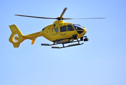 A yellow police helicopter coming in to land against a clear blue sky. Space for text in the sky.