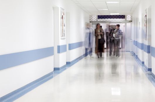 blurred figures of doctor and patients walking in a hospital corridor