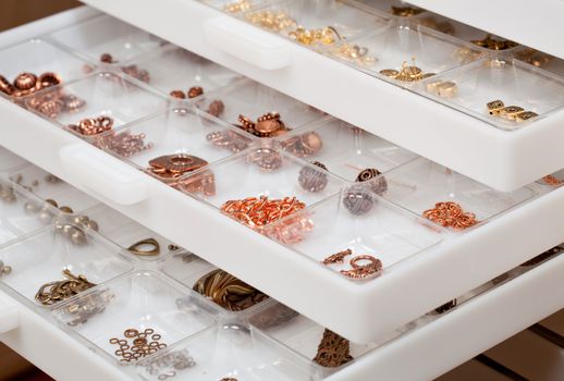 Small metal parts used to create home made jewelry and stored in white plastic drawers