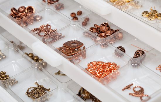 Small metal parts used to create home made jewelry and stored in white plastic drawers