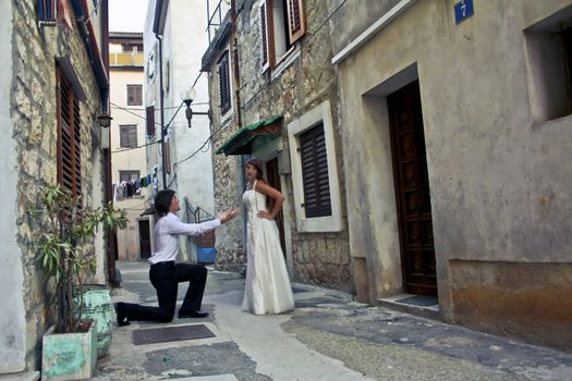 Young man romantically proposing to his pretty girlfriend on a small street of the old town