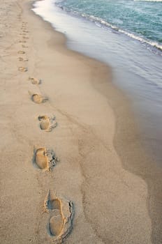 Foot imprints beside waves reaching margin at the seaside. Romantic stroll.