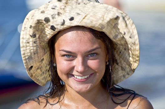 Close-up portrait of beautiful young cute smiling woman in a hat at the beach. Water droplets on the skin