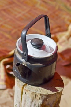 Sooty teapot is on the stump against the backdrop of colorful blankets on the beach. Summer, shallow depth of field.