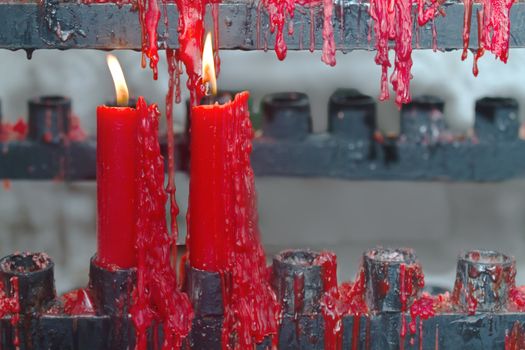 Photo of a pair of red candles burning in a temple shelf