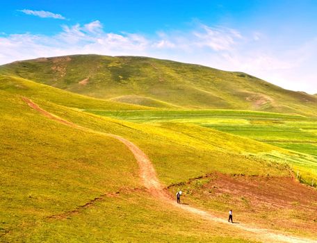 Landscape photo of pepole walking along a road in colorful plain and hills