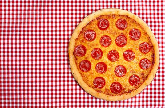 Whole pepperoni pizza on red gingham tablecloth with copy space.