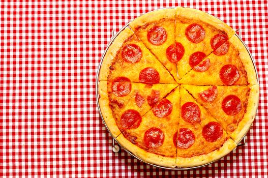 Sliced whole pepperoni pizza on red gingham tablecloth with copy space.