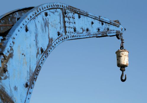 Very old rusty hook on a blue harbour crane against a clear blue sky. Focus on hook. Hamburg harbour.
