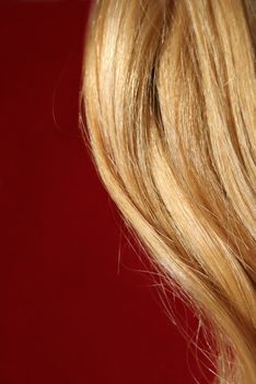 Blonde hair on wine-red background, lit by the sun. Warm colours.