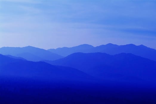 Abstract of mountains and hills at sunrise, in different shades of blue.