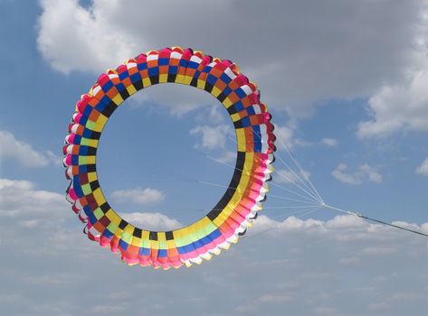 Very large, colourful, circular kite on a cloudy sky background.