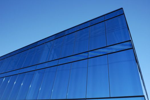 A modern office block with blue glass facade thrusts into the sky