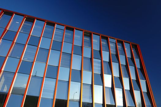 A glass-fronted office block, with little bits of the world reflected in the windows, against a clear blue sky