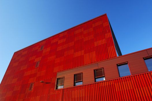 An orange factory building towers above the viewer, contrasting strongly with a clear blue sky