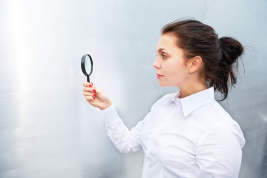 Young woman using magnifying glass outside building