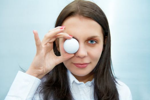 Young woman holding golf ball over eye