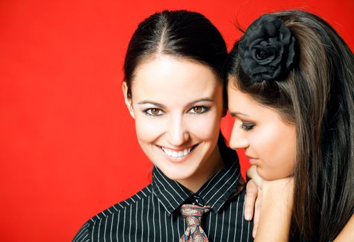 Two young females - one leaning on the others shoulder, red background