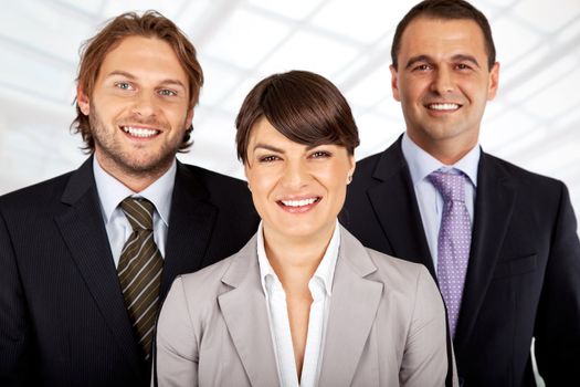 business team of three, female in front, two males behind, all smiling