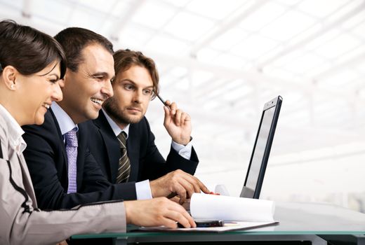 Team of three businesspeople sitting behind laptop, looking at the laptop, copyspace