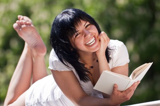 young female with white dress in the park with a book, laughing
