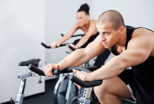 Young athletic couple spinning veloargometers in gym, male on focus