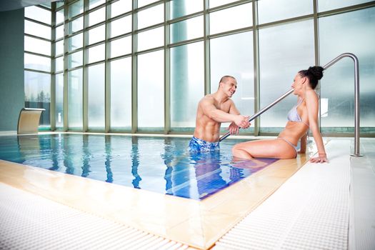 Young attractive couple chatting and playing in a swimming pool